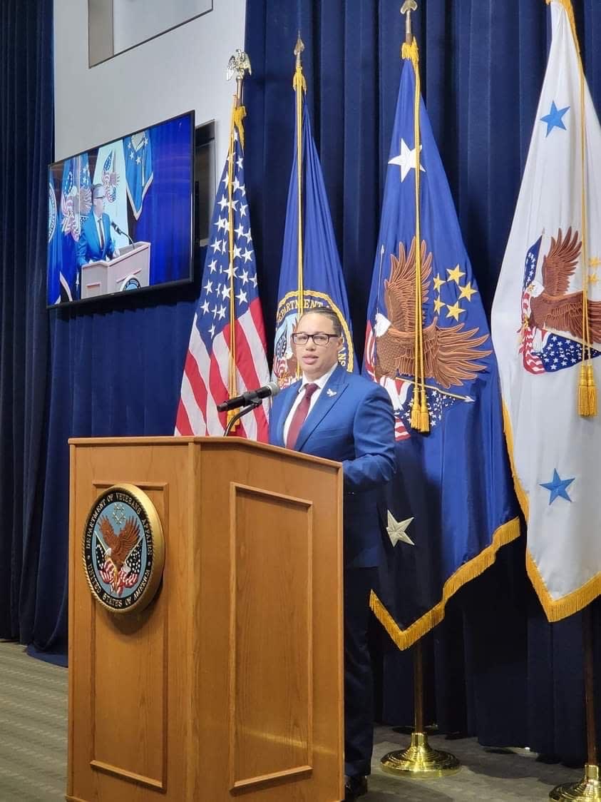A man standing at a podium in front of flags
